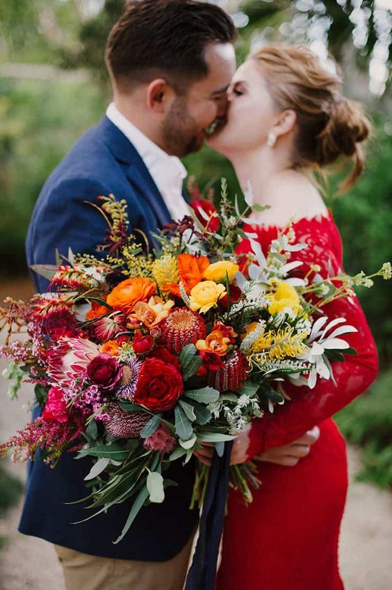 an amazing jewel tone wedding bouquet with orange, burgundy, yellow, pink and deep red blooms and greenery is wow
