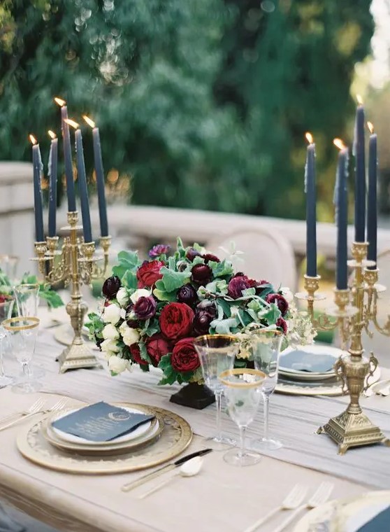 an elegant moody wedding centerpiece of white, ruby red and plum-colored blooms and greenery