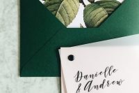 an emerald envelope with floral lining, a letterpress invitation and a vellum sheet on top with a black pin