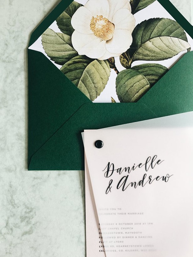 an emerald envelope with floral lining, a letterpress invitation and a vellum sheet on top with a black pin