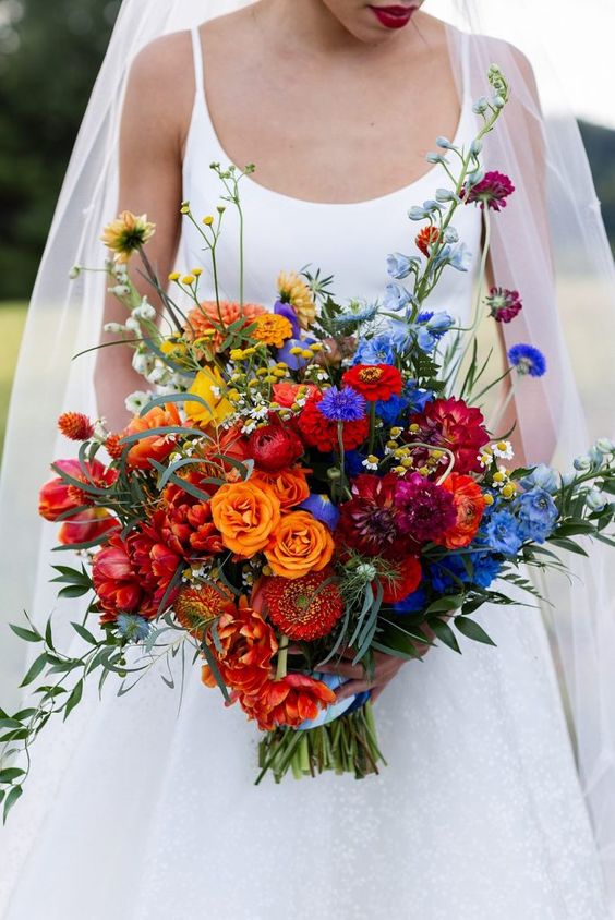 an extra bold wedding bouquet with burgundy and hot red blooms, orange and yellow ones, purple and blue, greenery is amazing for the fall
