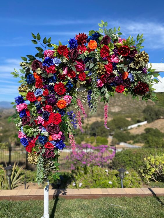 bold jewel tone wedding arch decor done with hot red, burgundy, bold blue and fuchsia blooms and greenery for a bright fall wedding