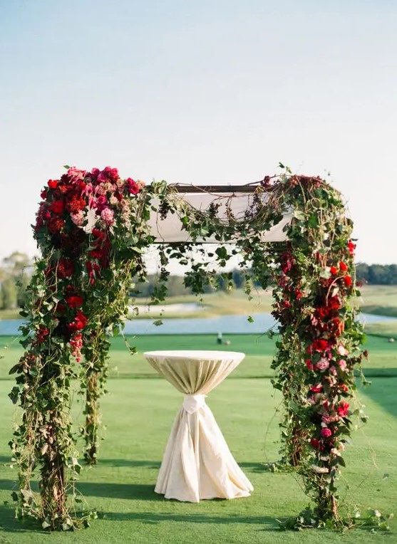 floral draped ceremony arbor with greenery, red, burgundy and pink blooms is a perfect fit for a jewel tone wedding
