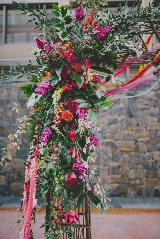 hot pink, red and orange flower arch decor with lush greenery is a great idea for a jewel tone wedding