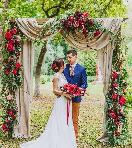 hot red and burgundy flowers on the arch with flowy fabric create a fantastic jewel tone wedding arch