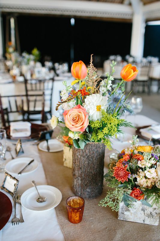 a colorful rustic wedding centerpiece of a tree stump with bold blooms and greenery and candles around is a lovely idea for a rustic wedding