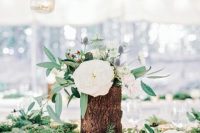05 a lovely cluster wedding centerpiece of textural greenery, tree stumps with white blooms, greenery and thistles and a candleholder
