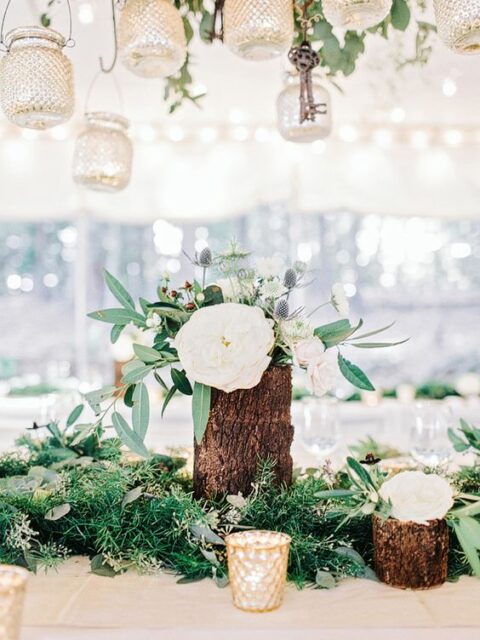 a lovely cluster wedding centerpiece of textural greenery, tree stumps with white blooms, greenery and thistles and a candleholder