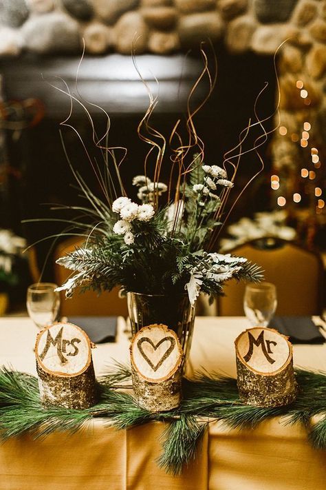 a rustic winter wedding centerpiece of evergreens, white blooms and twigs, cut tree stumps with monograms and evergreens