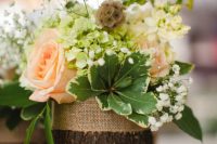 12 a rustic wedding centerpiece of a tree stump, with baby’s breath, greenery, seed pods and blush roses is a cool solution