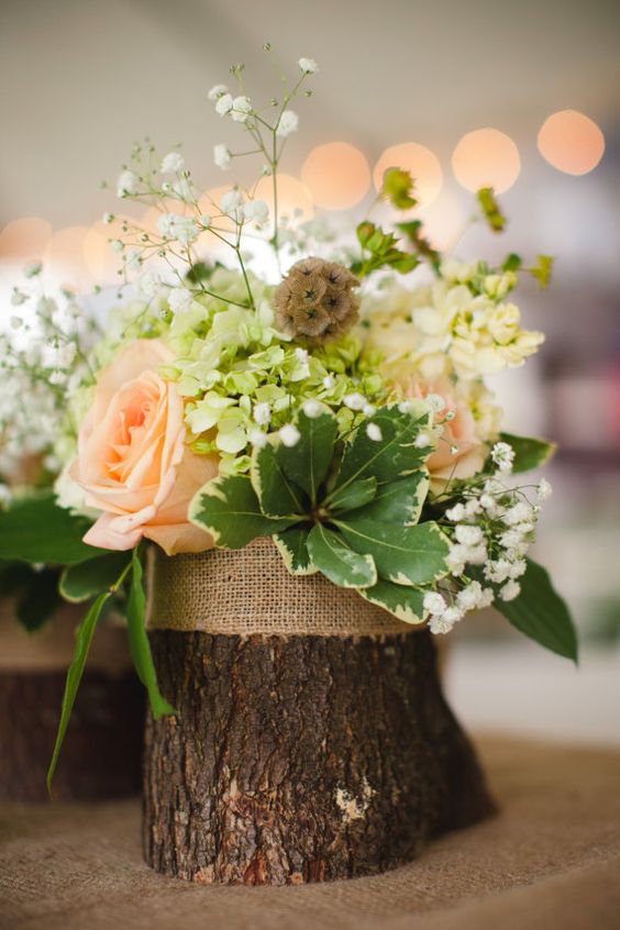 a rustic wedding centerpiece of a tree stump, with baby's breath, greenery, seed pods and blush roses is a cool solution
