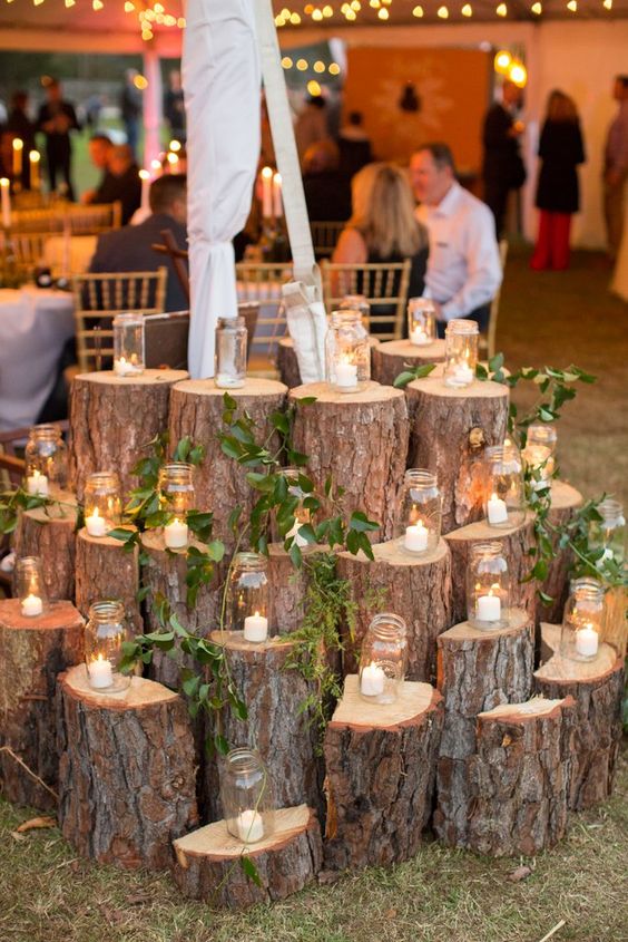 a large rustic wedding decoration made of tree stumps with greenery and candle lanterns is a cool idea to rock
