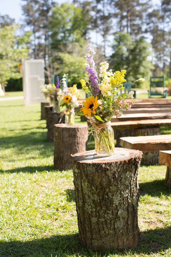 a rustic wedding aisle styled with tree stumps and bold floral arrangements is a stylish idea for a rustic or boho wedding