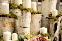a rustic wedding candle display made of tree stumps and logs, moss and pillar candles and some blooms is a lovely idea