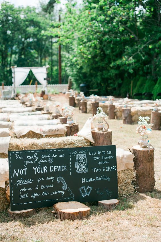 a rustic wedding ceremony space with hay, tree stumps, tree slices and a large chalkboard is a cool idea for a rustic wedding