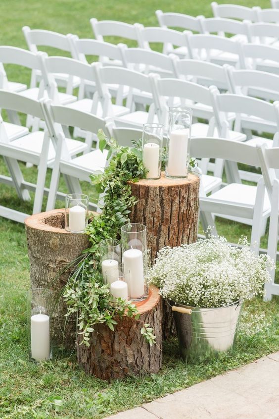 a rustic wedding decoration of tree stumps, greenery and candles plus a bucket with baby's breath is a cool piece to DIY for a wedding