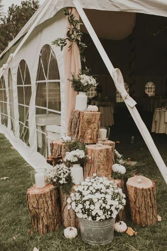 a rustic wedding decoration of tree stumps, mini pumpkins, candles and white bloom arrangements is a cool idea for a wedding