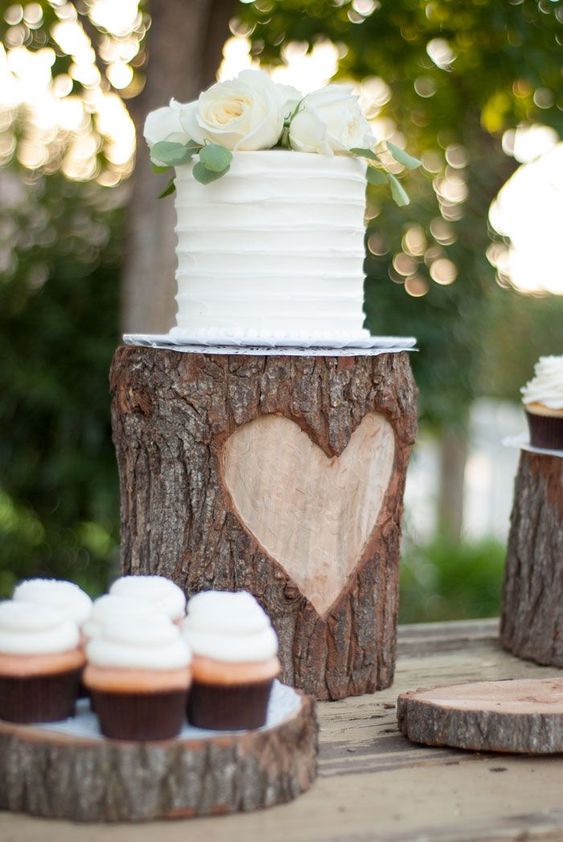 a rustic wedding dessert table done with a tree stump with a white wedding cake and tree slices as holders for desserts is a lovely idea