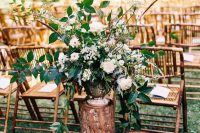 33 a stylish rustic wedding ceremony space with rattan chairs, tree stumps holding a large white flower arrangement with greenery is wow
