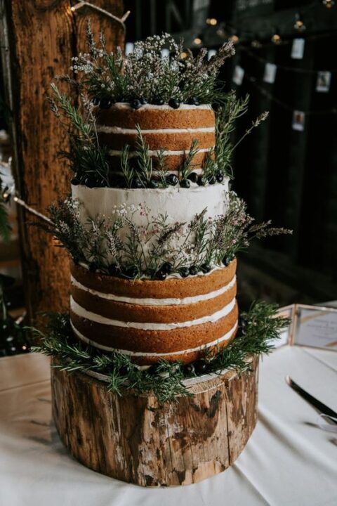 a tree stump as a stand for a gorgeous naked and buttercream wedding cake decorated with berries and wildflowers