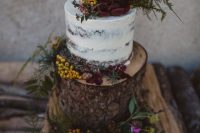 35 a tree stump decorated with greenery, bold blooms and pinecones, some berries as a stand for a naked wedding cake topped with the same decor