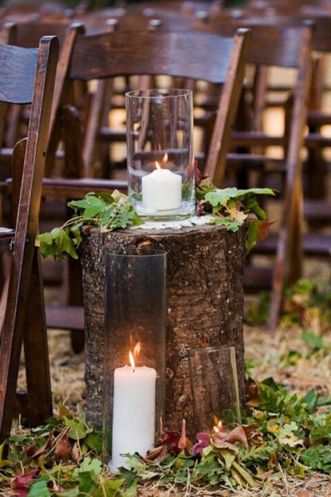 fall aisle decor with a tree stump, with large candleholders, green and dark foliage is a pretty rustic idea, you can DIY such an aisle easily