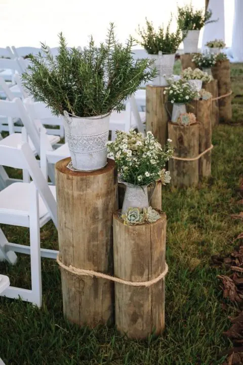 rustic wedding aisle decor with tree stumps secured with rope, succulents, greenery in buckets, vintage jugs with wildflowers