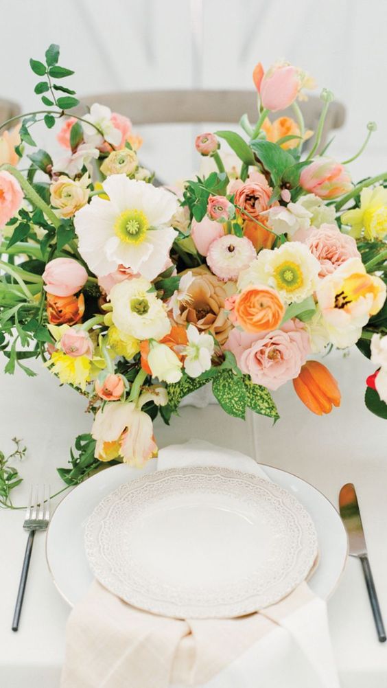 a beautiful and vivacious wedding centerpiece of white poppies, blush roses and peony roses, orange tulips and greenery