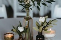 a beautiful cluster wedding centerpiece of a cleat bottle and apothecary ones, candles, greenery and white blooms is a cool solution for a boho wedding