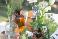 a boho cluster wedding centerpiece of apothecary bottles, greenery and wildflowers, berries and some clear glasses is super cool