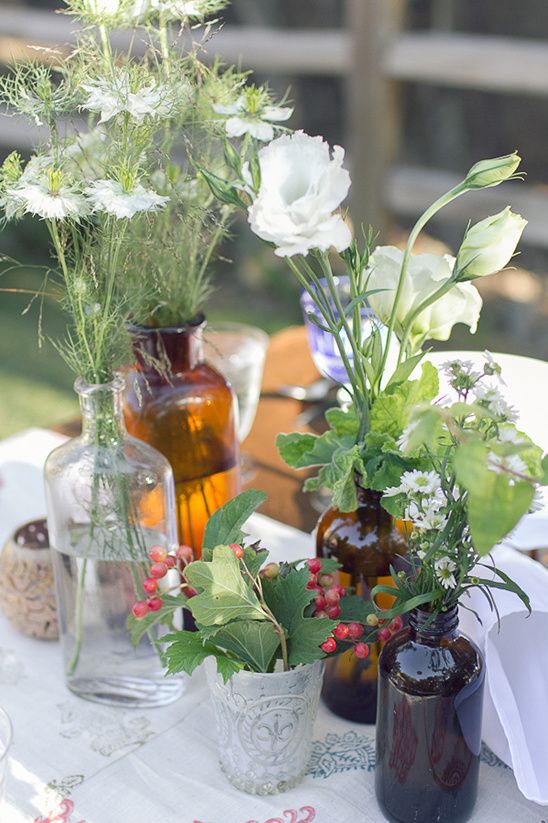 a boho cluster wedding centerpiece of apothecary bottles, greenery and wildflowers, berries and some clear glasses is super cool