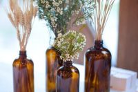 a boho cluster wedding centerpiece of apothecary bottles, wheat, greenery and waxflower is a cool decoration to DIY