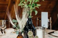 a boho wedding centerpiece of apothecary bottles, a candle, wheat and greenery for a simple look