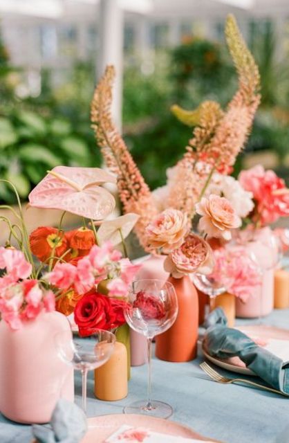 a bright cluster wedding centerpiece of red poppies and roses, pink roses, peony roses and other blooms in colorful vases