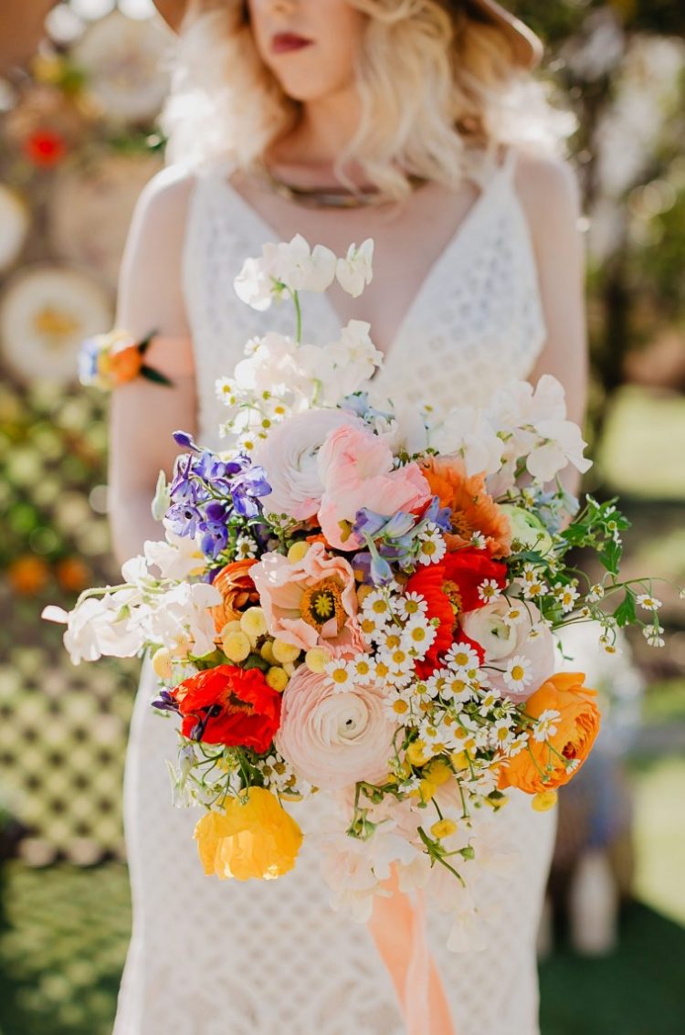 a bright wedding bouquet of yellow and pink poppies, pink ranunculus, white and lilac blooms, chamomiles and long peachy ribbon