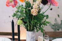 a bright wedding centerpiece of a marble vase, red and orange poppies, blush and deep purple blooms and greenery