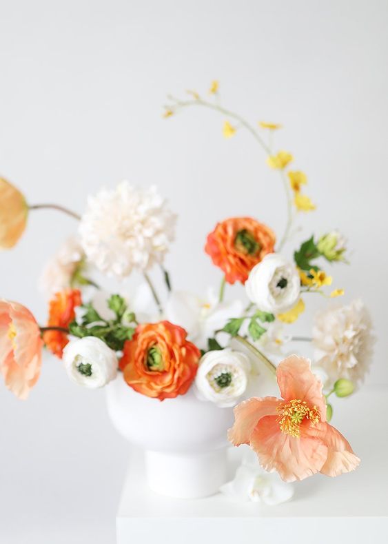 a bright wedding centerpiece of white and coral blooms, yellow ones and greenery looks artful and very exquisite