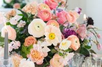 a bright wedding centerpiece of white and orange ranunculus, pink peonies and roses, greenery and candles around