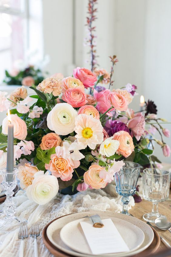 a bright wedding centerpiece of white and orange ranunculus, pink peonies and roses, greenery and candles around