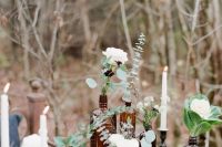 a catchy wedding centerpiece of apothecary bottles placed on stands and with white blooms and greenery in them