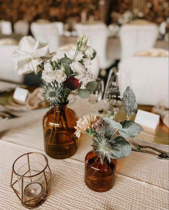 a cluster wedding centerpiece of apothecary bottles, greenery and thistles, neutral blooms and candles around is a cool idea for a boho wedding