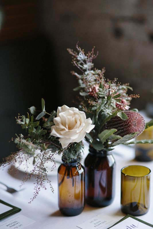 a cluster wedding centerpiece of apothecary bottles with neutral and pink blooms, greenery and berries is a cool idea to rock