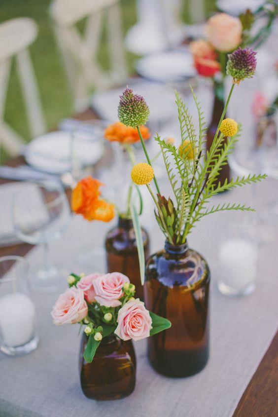 a cluster wedding centerpiece of apothecary bottles with pastel and bright blooms and greenery is a lovely idea for spring or summer