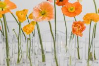 a cluster wedding centerpiece of glass vases and yellow ranunculus and orange and yellow poppies, one bloom in each vase