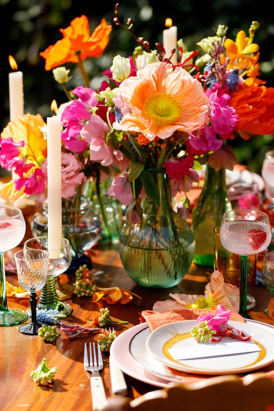 a colorful summer wedding centerpiece of orange and yellow poppies, pink, fuchsia, blue and hot pink blooms and candles for a festival wedding