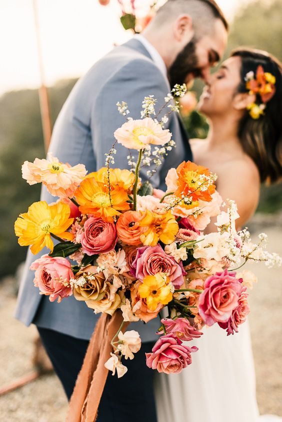 a colorful wedding bouquet of bold yellow and light pink poppies, pink and coffee-colored roses, pink and orange ranuculus and some fillers
