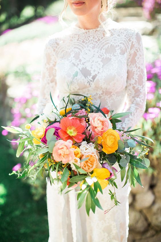 a colorful wedding bouquet of pink and yellow ranunculus, red and yellow poppies, greenery and billy balls is amaizng for a summer bride