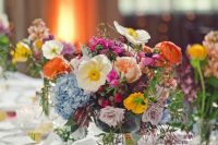 a colroful wedding centerpiece of yellow and white poppies, lue hydrangeas, orange ranunculus and lilac roses is wow