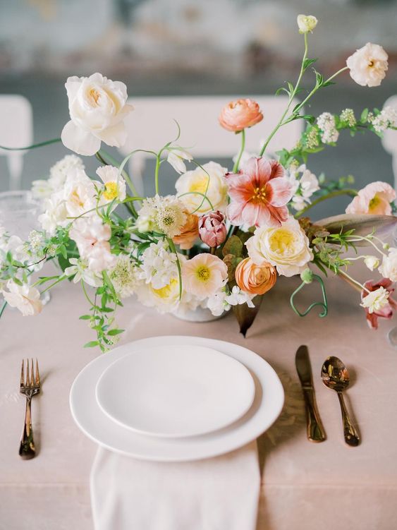 a delicate and refined wedding centerpiece of white peony roses, blush and pink poppies, yellow and orange blooms and greenery