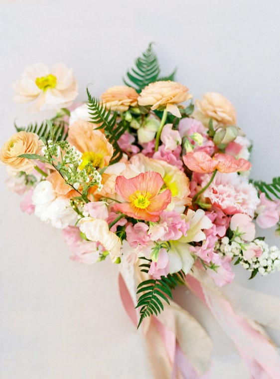 a dreamy pastel wedding bouquet of pink and yellow poppies, yellow and pink ranunculus, greenery and long ribbon is wow